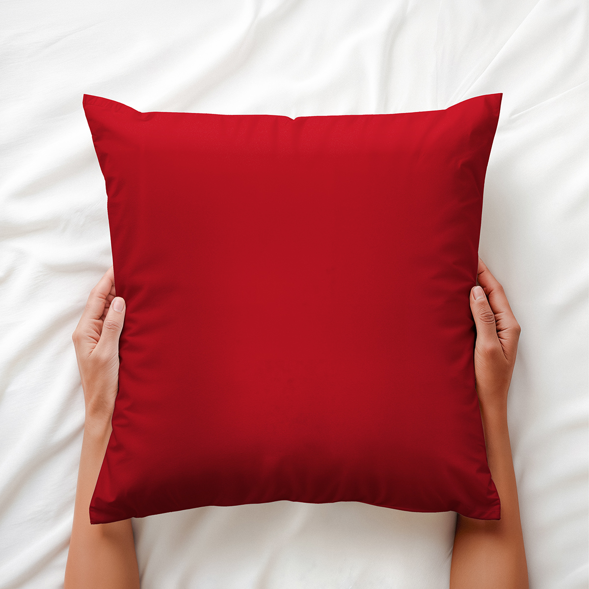 Miękka czerwona poduszka dekoracyjna trzymana w dłoniach na białej pościeli
