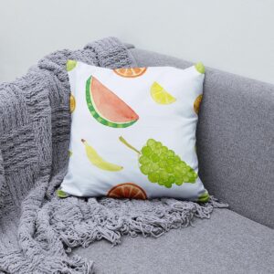 Poduszka ozdobna na kanapie obok szarego koca, motyw banana i plasterków cytrusów