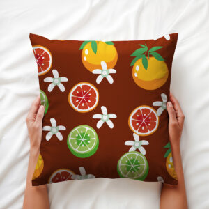 Poduszka trzymana w dłoniach, widoczne detale nadruku z zielonymi limonkami, czerwonym grejpfrutem i białymi kwiatami