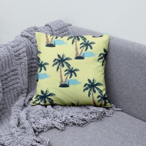Poduszka dekoracyjna z palmami ułożona na kanapie obok pledu