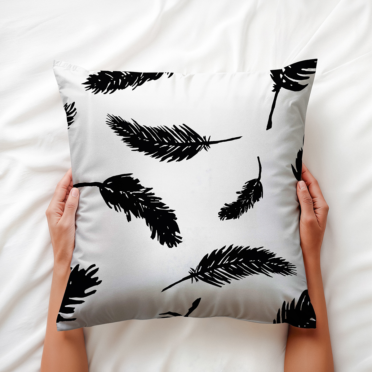 Ręce trzymające poduszkę z motywem piór, aranżacja na jasnej pościeli