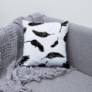 Poduszka ozdobna z wzorem czarnych piór na kanapie obok szarego koca