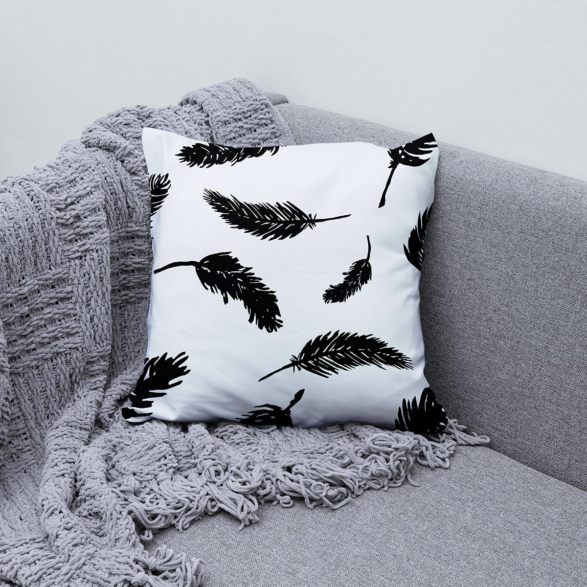 Poduszka ozdobna z wzorem czarnych piór na kanapie obok szarego koca
