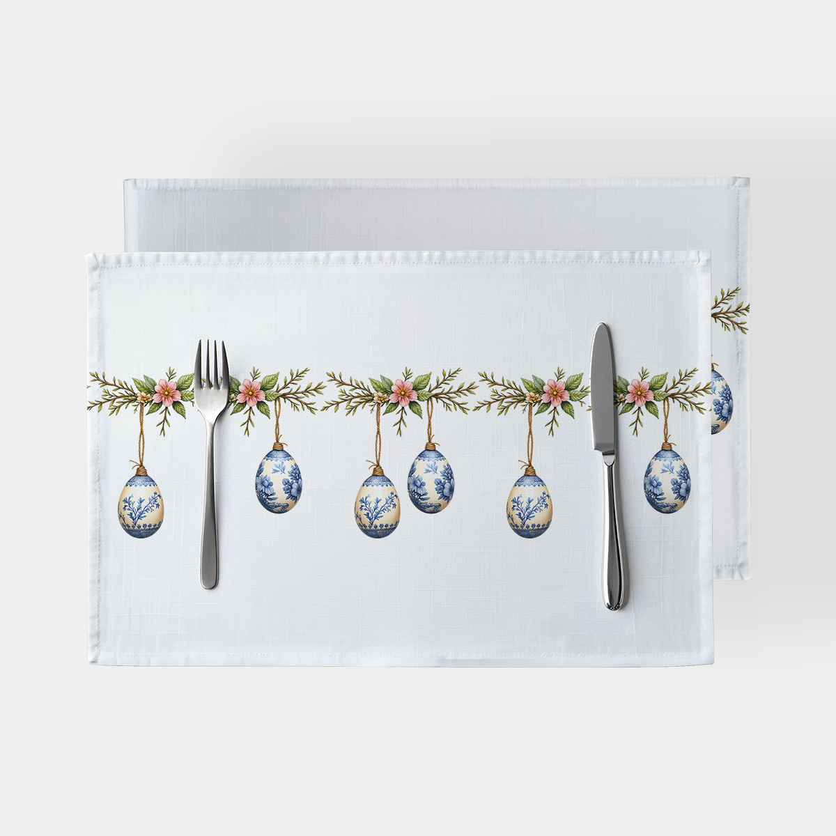 biała podkładka z gałązką i zawieszonymi porcelanowymi pisankami na stole, widok z góry z sztućcami