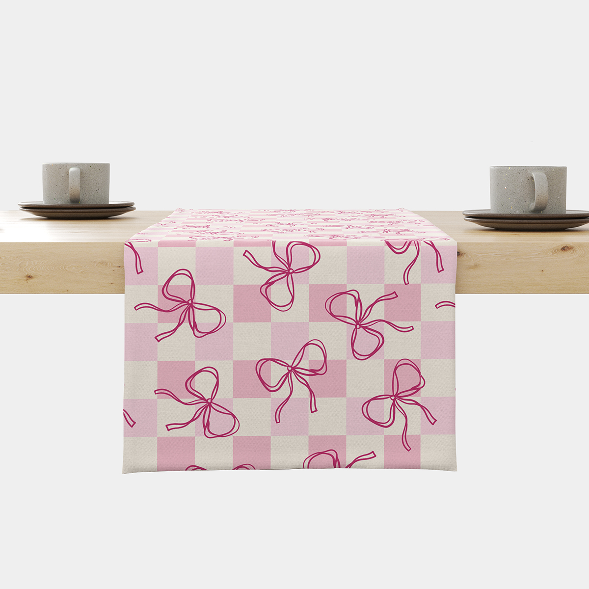 Bieżnik z pudrową kratką i różowymi kokardkami rozłożony na stole, widok z przodu