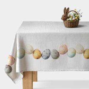 Biały obrus na stole z pasem pastelowych pisanek i złotymi plamkami, udekorowany koszykiem z jajkami