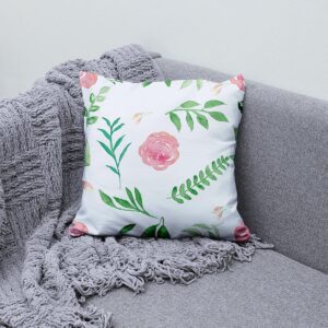 Poduszka akcentowa z różami i listkami ułożona na szarej sofie obok pledu, aranżacja wnętrza
