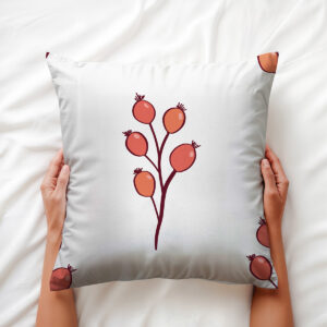 Dekoracyjna poduszka trzymana dłońmi, widoczny wzór czerwonych owoców i ciemna gałązka