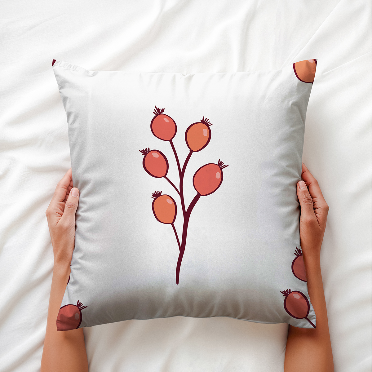 Dekoracyjna poduszka trzymana dłońmi, widoczny wzór czerwonych owoców i ciemna gałązka
