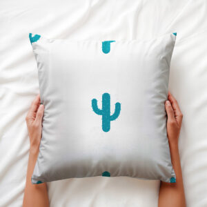 zbliżenie na poduszkę trzymaną w dłoniach pokazujące wzór turkusowego kaktusa