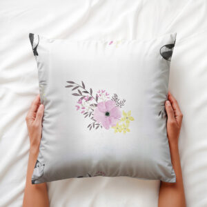 Ręce trzymają poduszkę z różowym akwarelowym kwiatem i dyskretnym lisiem przy rogu