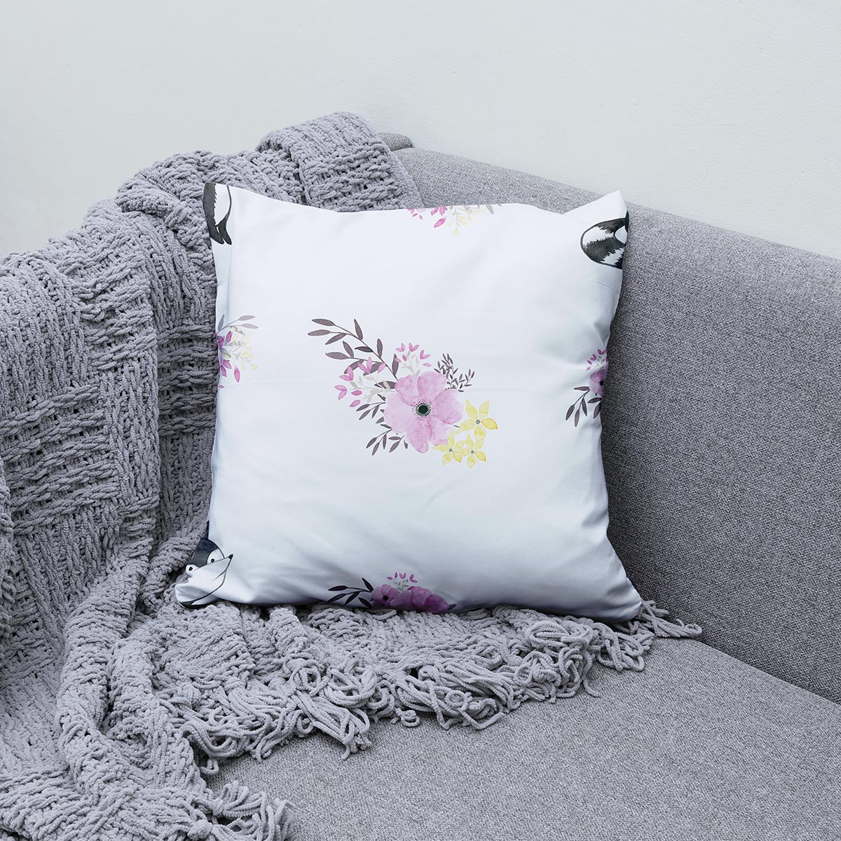 Poduszka ozdobna z liskiem i pastelowym bukietem ustawiona na kanapie z kocem