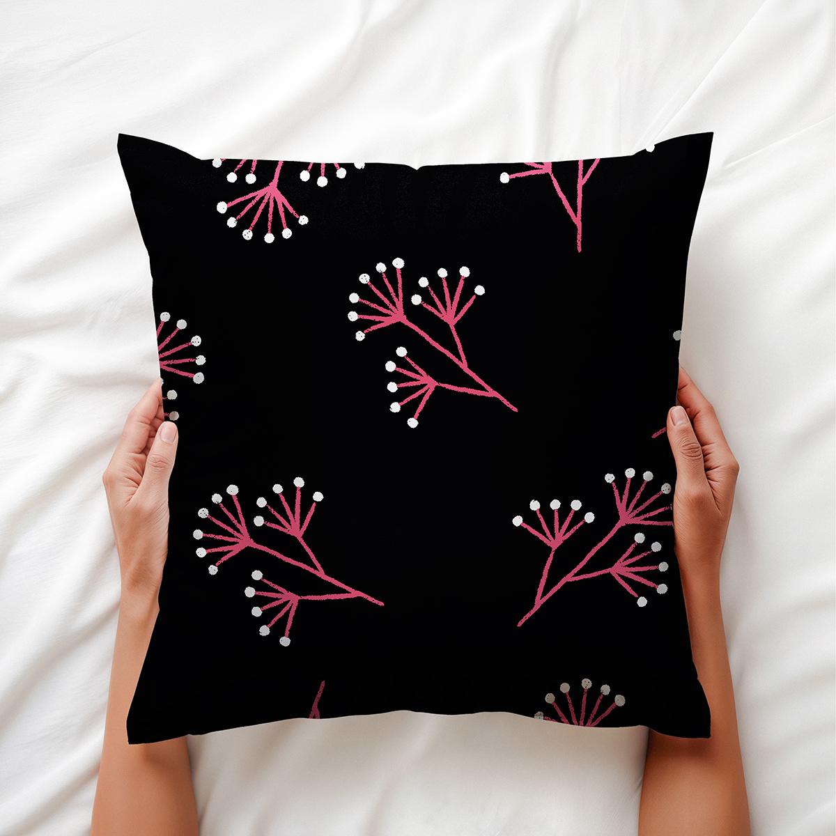 Ręce trzymające poduszkę z różowymi gałązkami na białej pościeli, aranżacja produktu