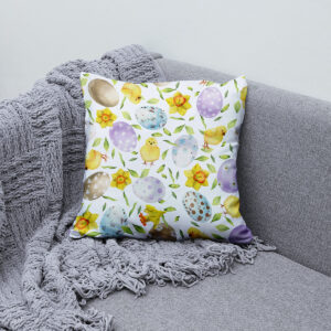 Poduszka ułożona na szarej sofie jako dekoracja z pastelowymi jajkami i żonkami