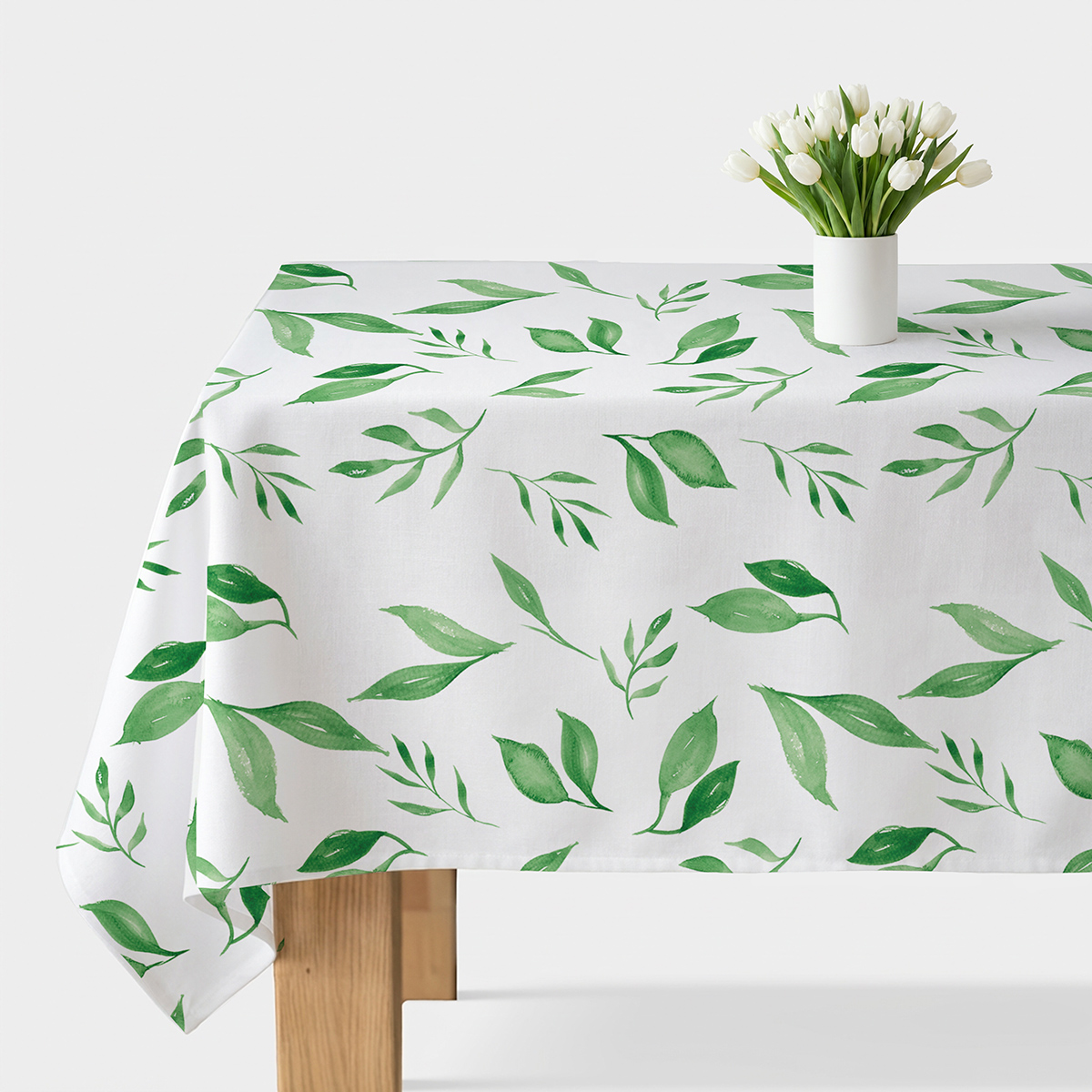 Obrus z akwarelowymi zielonymi listkami ułożony na stole z białym wazonem i tulipanami