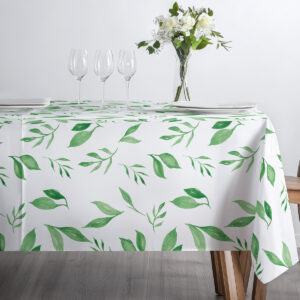 Detal stołu z obrusem, ustawione szkło i talerze na tle zielonych liści