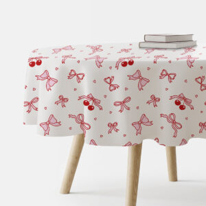 Okrągły obrus z wzorem czerwonych kokardek i wisienek na jasnym tle rozłożony na stole