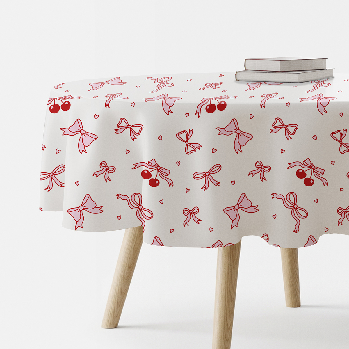 Okrągły obrus z wzorem czerwonych kokardek i wisienek na jasnym tle rozłożony na stole