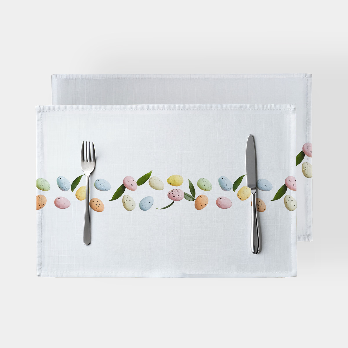 Białe podkładki ze wzorem pastelowych pisanek i zielonych listków, widok z góry