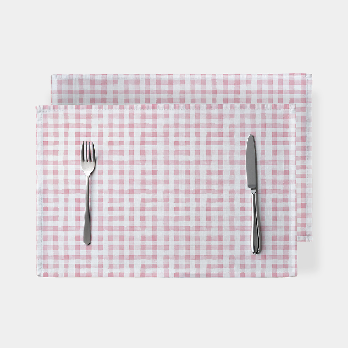 Podkładki w różową kratkę ułożone jedna na drugiej z widelcem i nożem