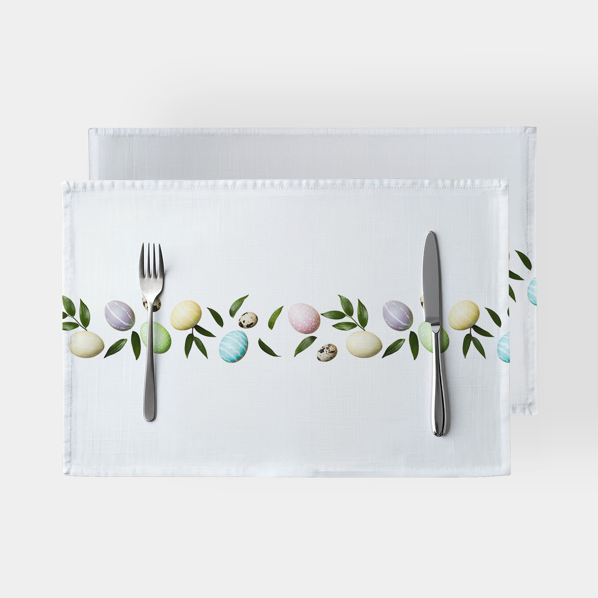Główne ujęcie białej podkładki z pasem pastelowych pisanek i zielonych listków