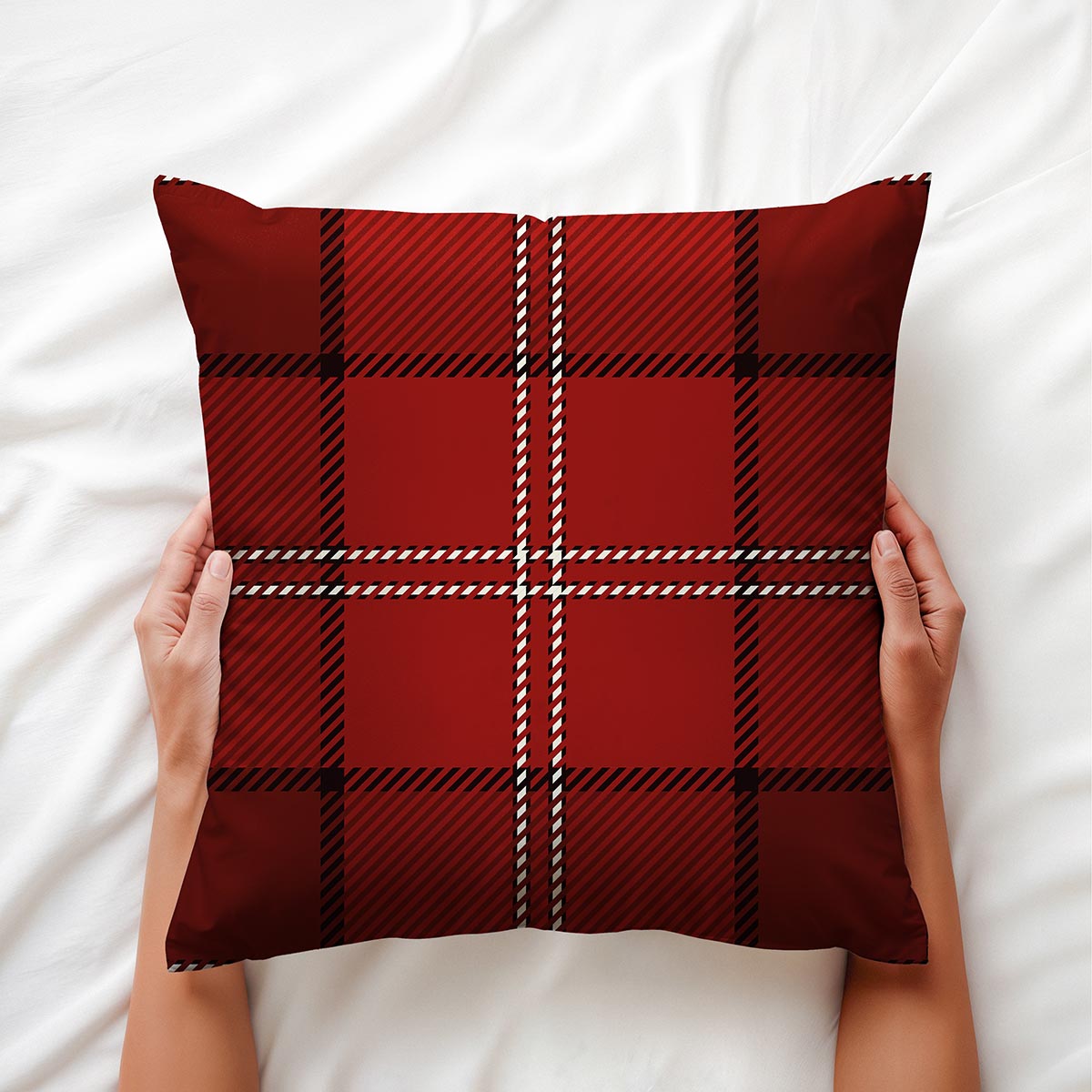 Ręce trzymające czerwoną poduszkę w kratę na białej pościeli, widok z góry