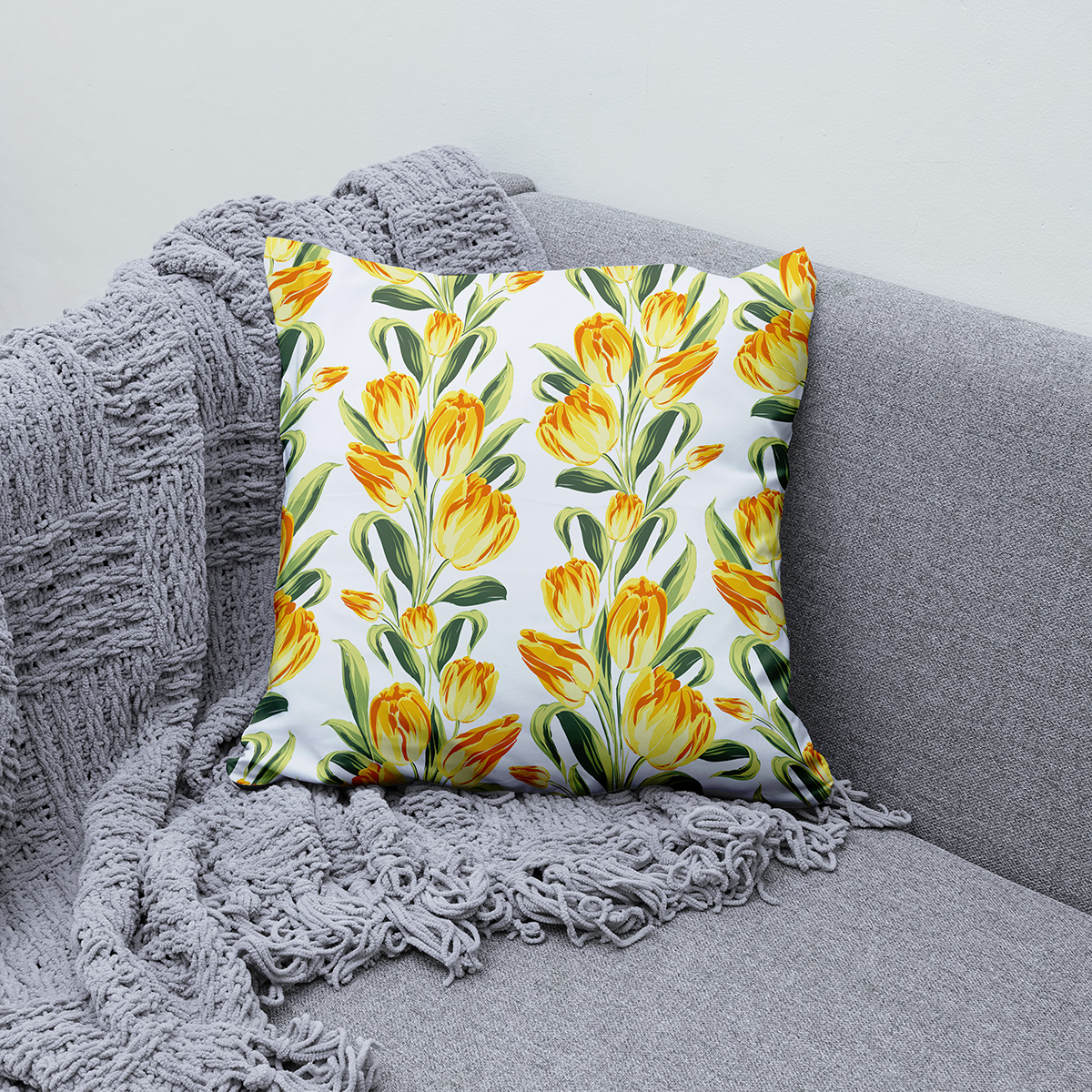 Poduszka ułożona na szarej sofie, stylizacja wnętrza z wiosennym akcentem