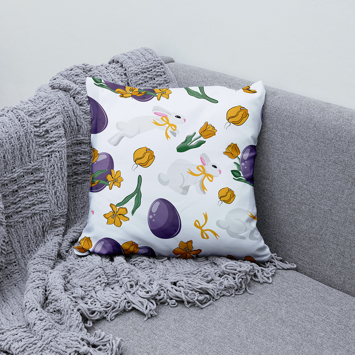 Poduszka z wiosennym wzorem ułożona na kanapie obok szarego koca