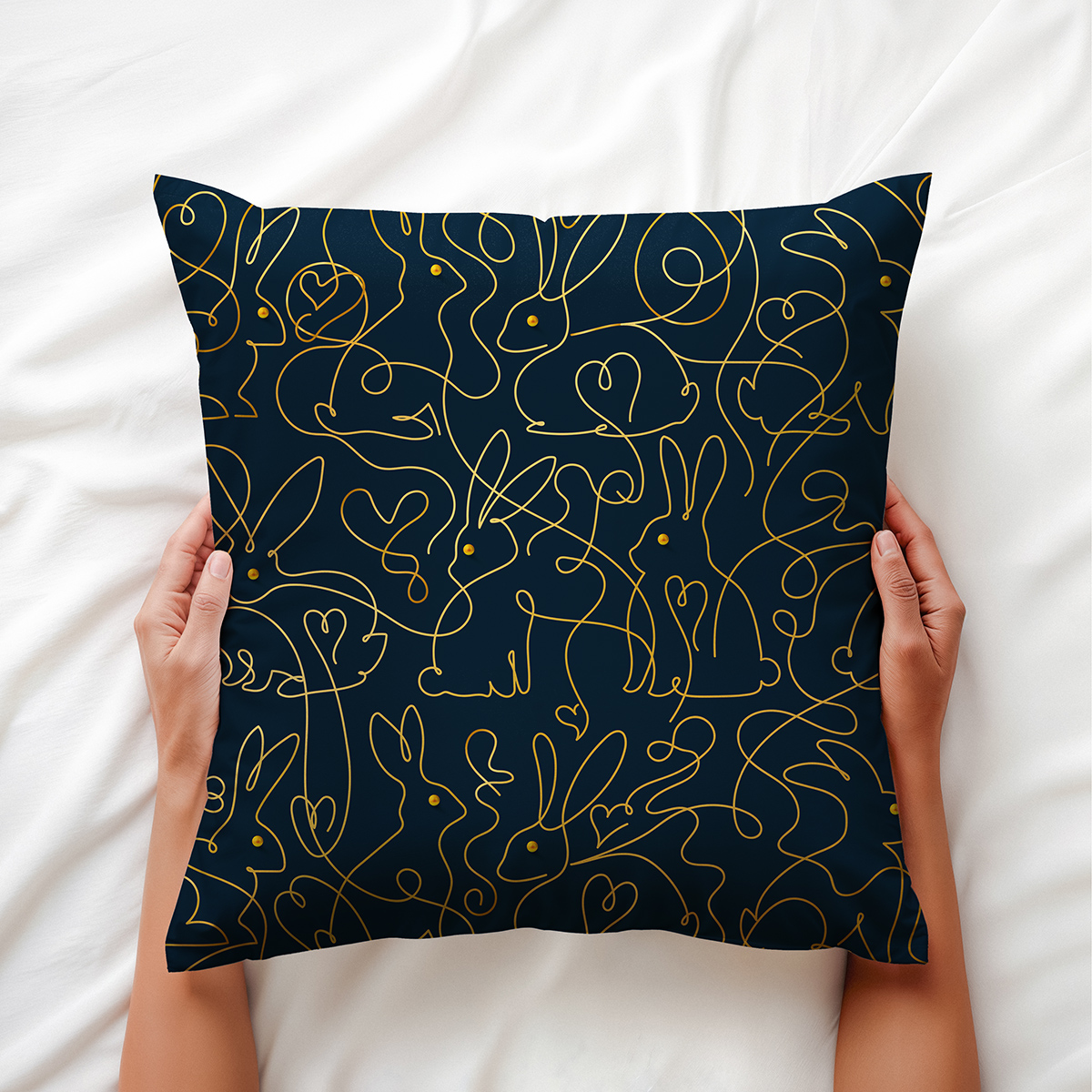 ręce trzymające poduszkę na białej pościeli, widoczny złoty motyw króliczków