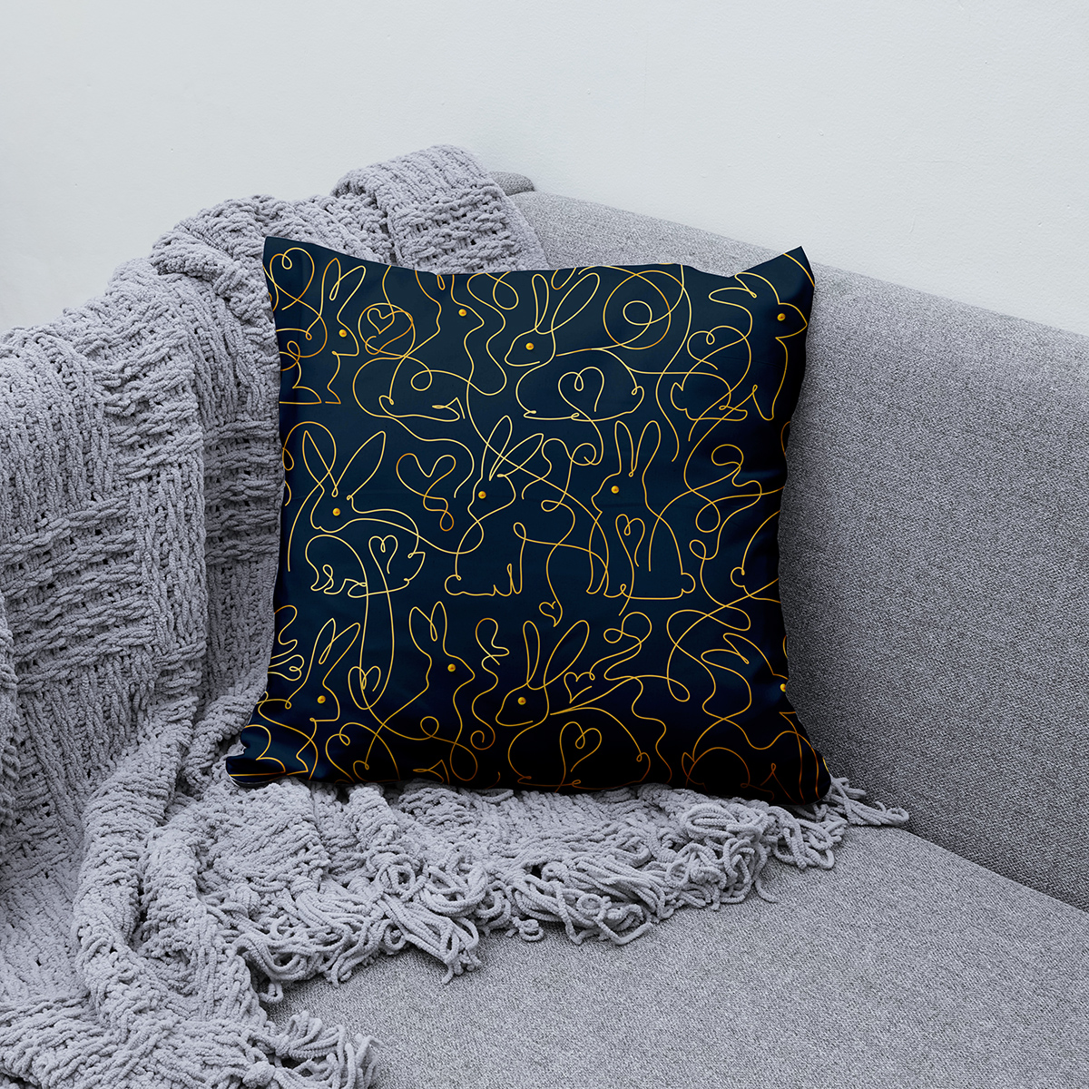 poduszka ustawiona na kanapie obok szarego koca, detal złotych linii