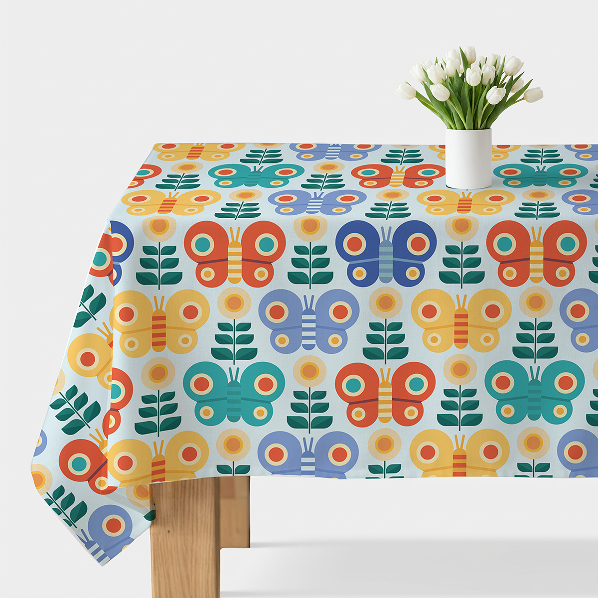 Obrus na stole z wzorem kolorowych motyli i stylizowanych kwiatów, widok ogólny z wazonem tulipanów