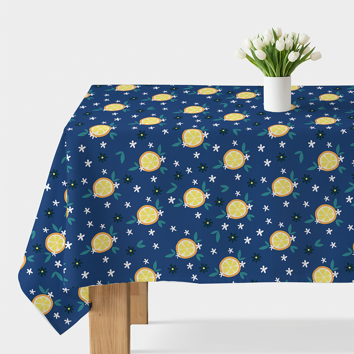 Obrus z motywem cytryn na granatowym tle rozłożony na stole z wazonem tulipanów