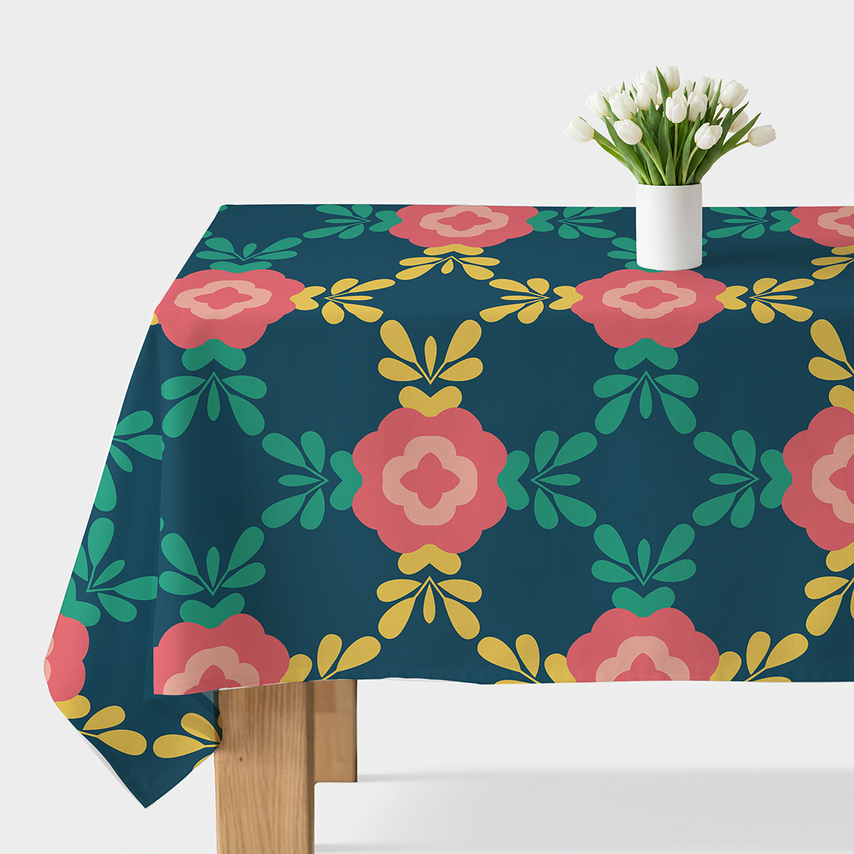 Obrus rozłożony na stole z widocznym wzorem dużych koralowych kwiatów i wazonem z białymi tulipanami