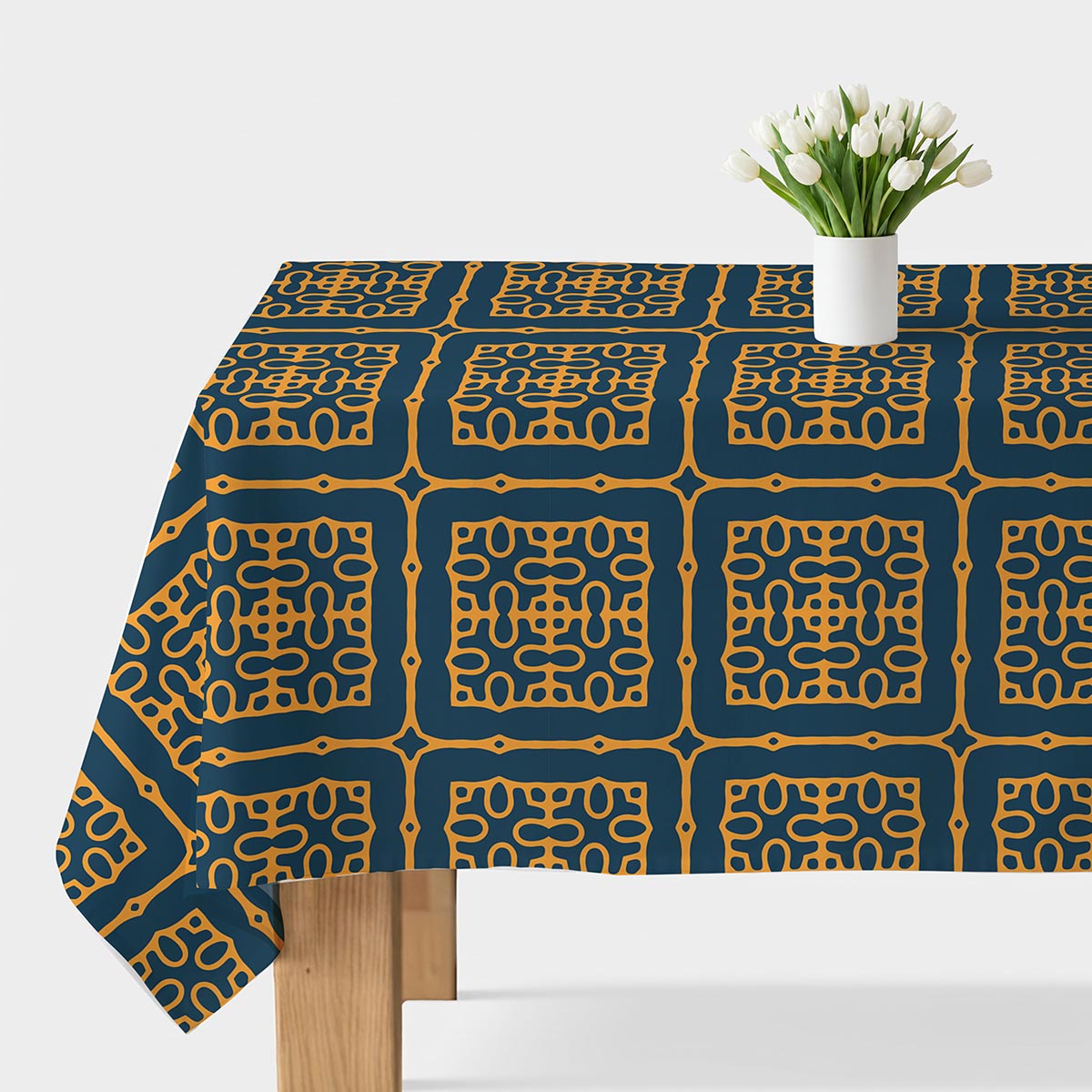 Obrus z kafelkowym musztardowym ornamentem na granatowym tle, widok stołu z wazonem białych tulipanów
