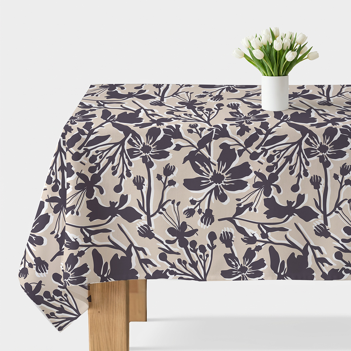 Obrus na stole z beżowym tłem i grafitowym motywem kwiatowym, na środku biały wazon z tulipanami