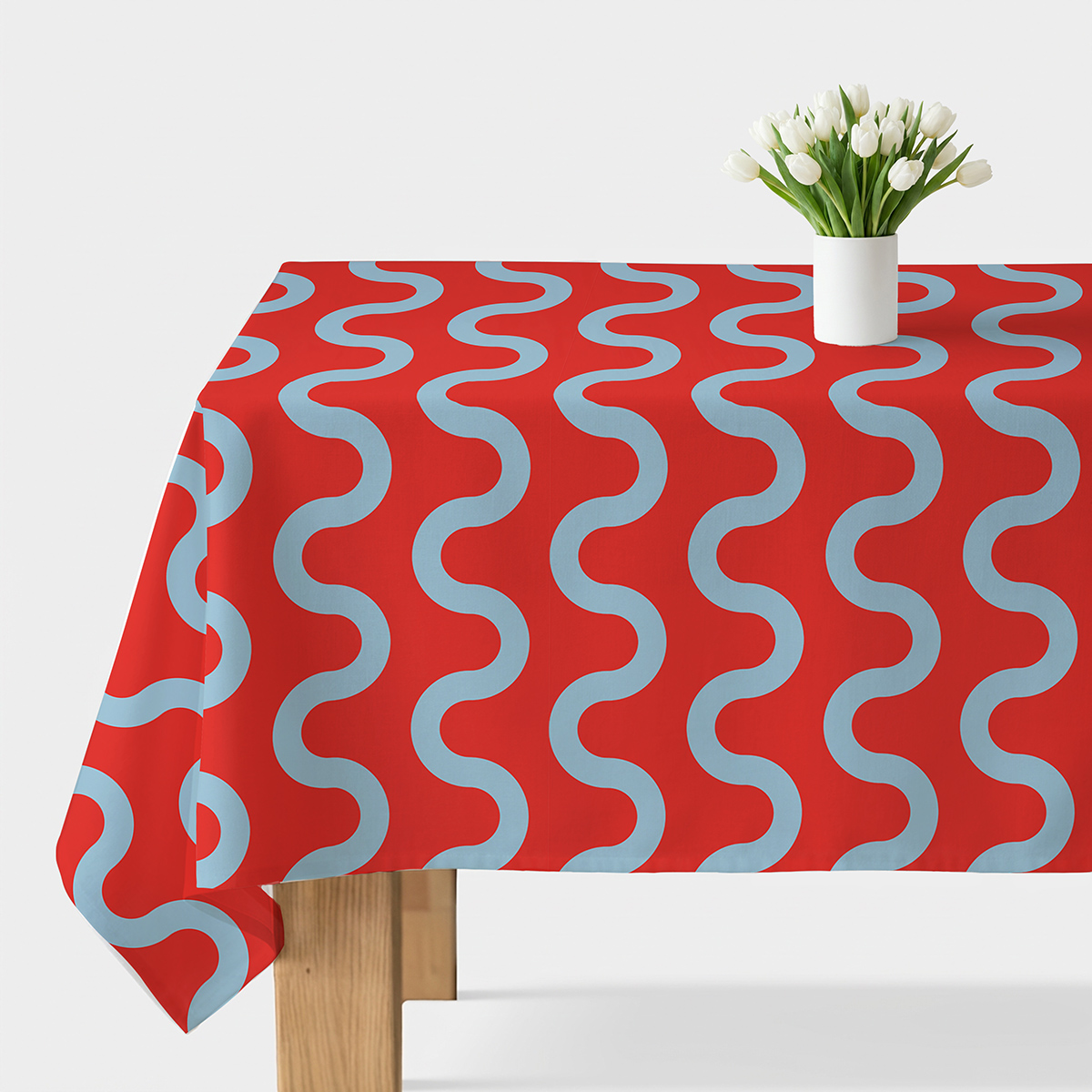 obrus czerwony z błękitnymi falami ułożony na stole z białym wazonem tulipanów