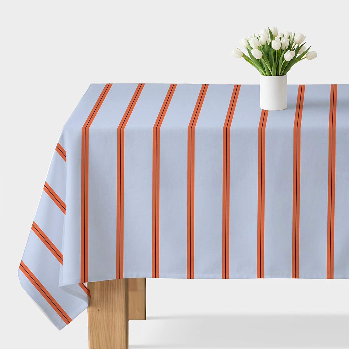 Obrus na stole jasnoniebieski z pionowymi pomarańczowymi pasami i wazon z białymi tulipanami
