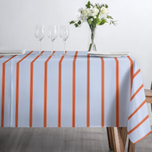 Widok stołu od przodu z obrusem jasnoniebieskim i pomarańczowymi pasami, kieliszki i talerz
