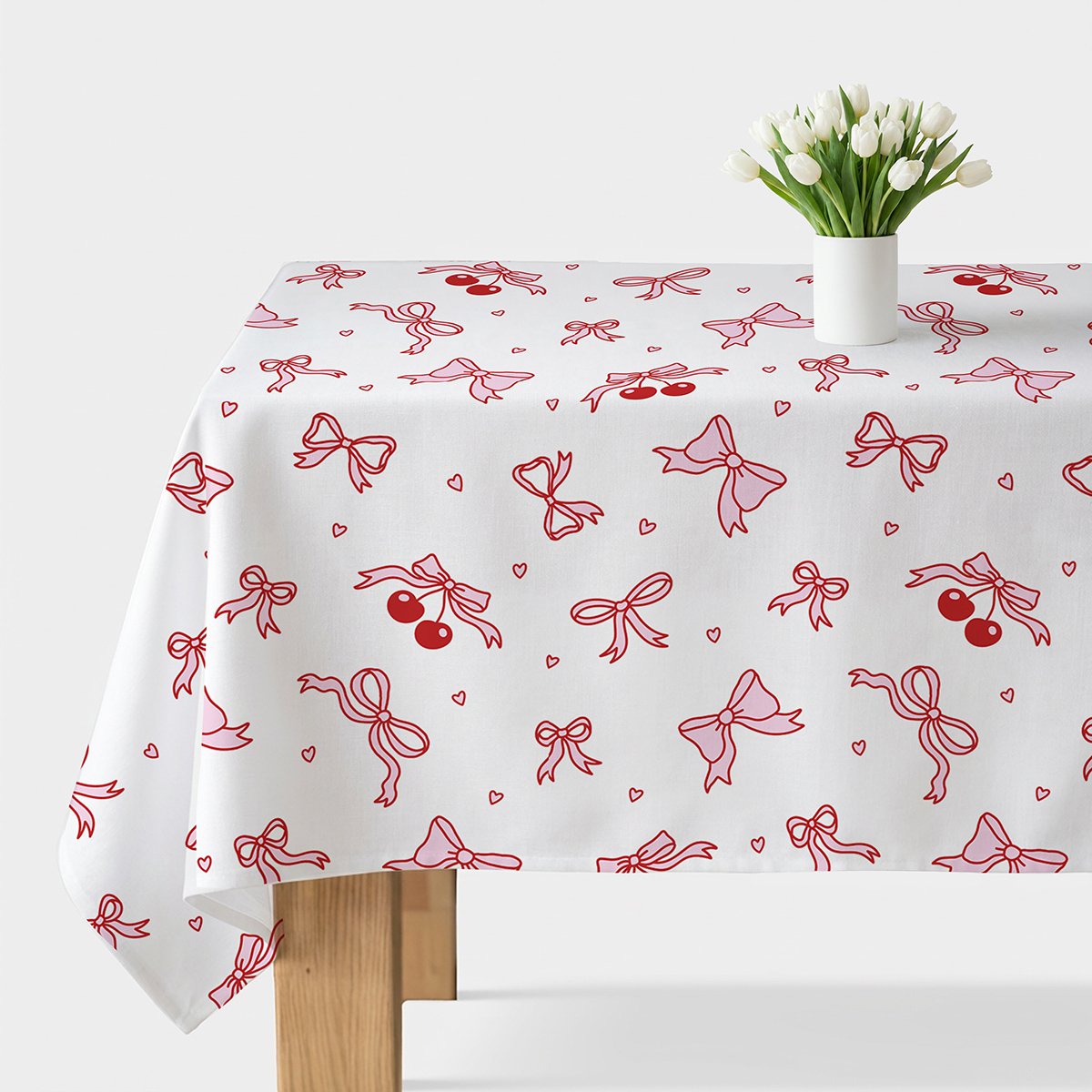 obrus na stole z białym wazonem tulipanów, wzór z kokardkami i wiśniami