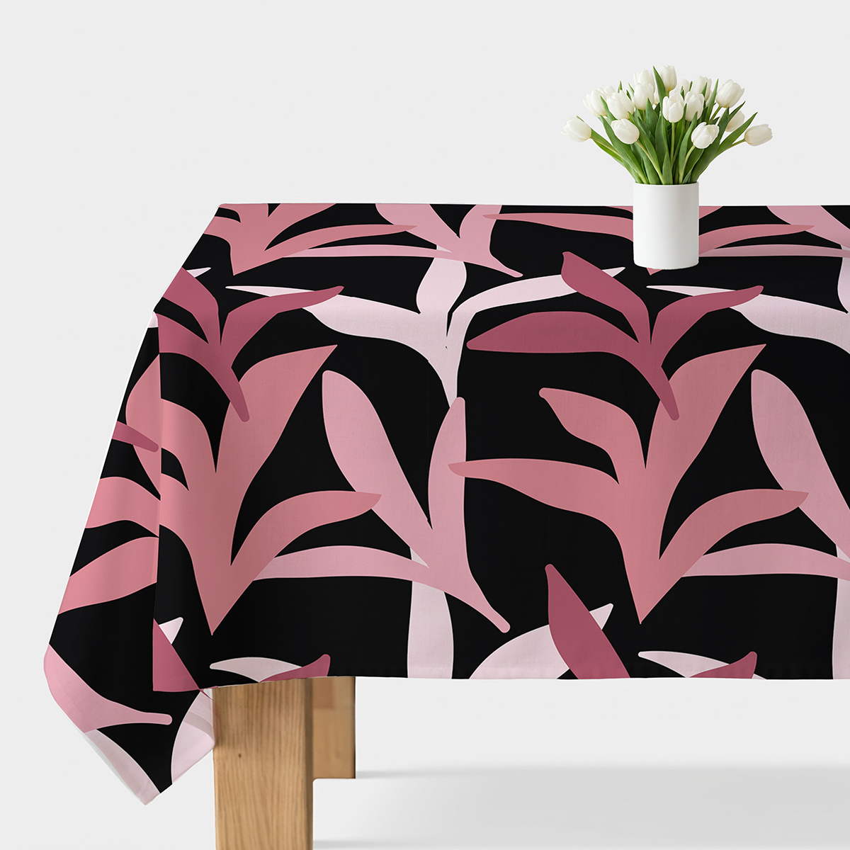 obrus z różowo-malinowymi liśćmi na czarnym tle ułożony na stole z białym wazonem i tulipanami