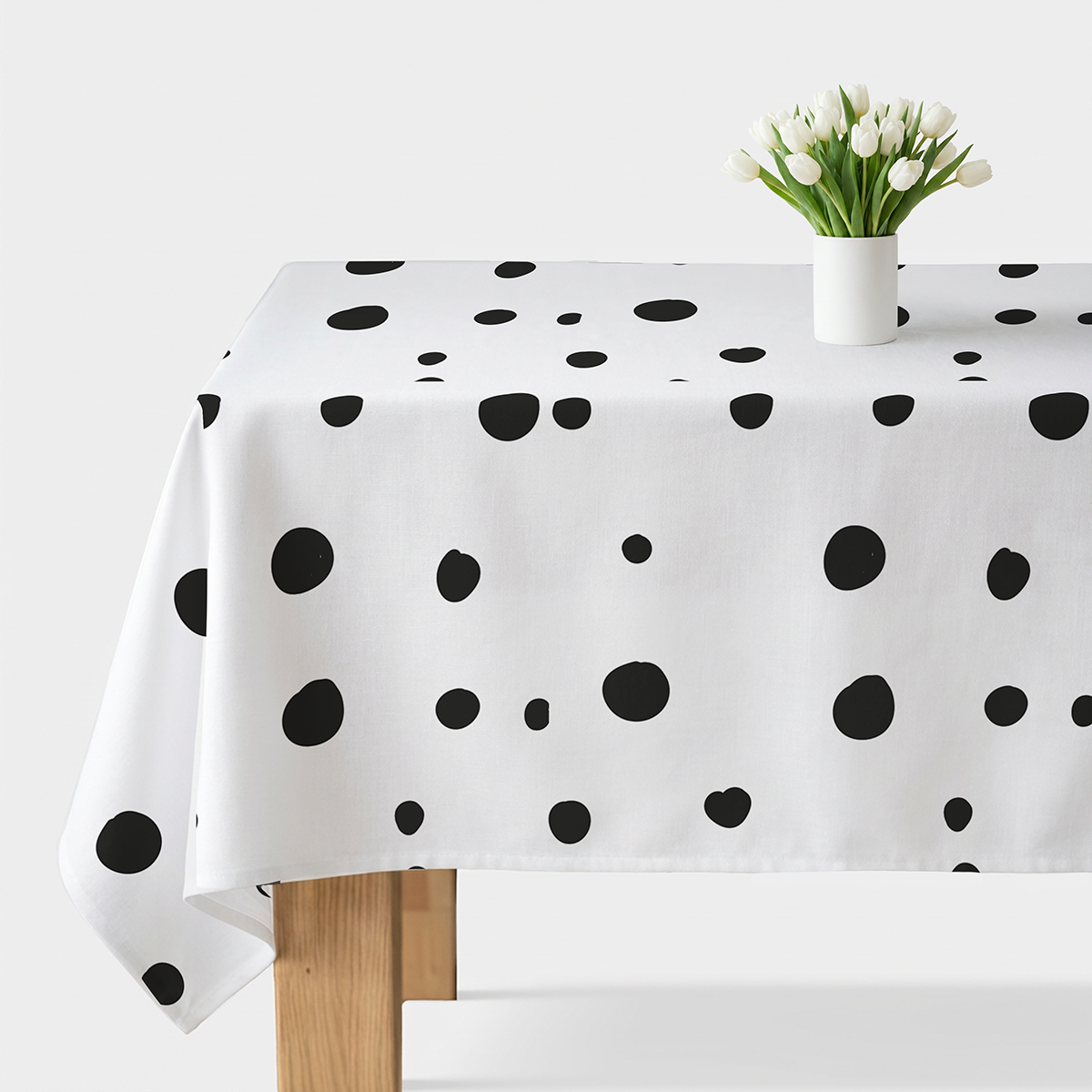 Obrus biały z nieregularnymi czarnymi grochami na stole z wazonem białych tulipanów