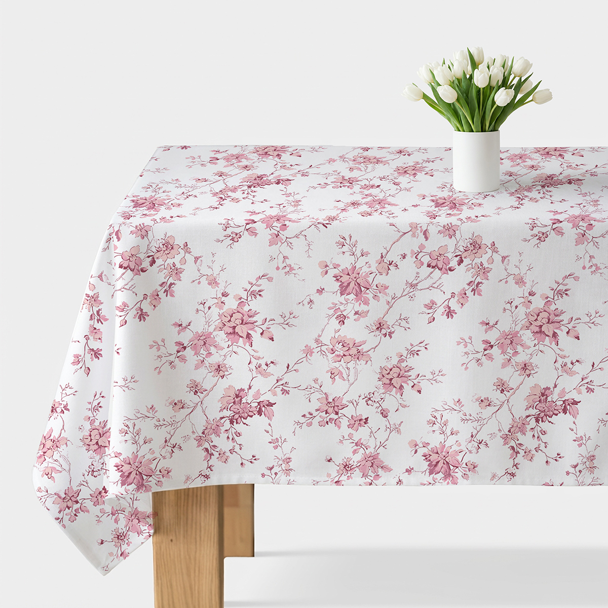 Stół nakryty białym obrusem z różowymi gałązkami, na środku biały wazon z białymi tulipanami