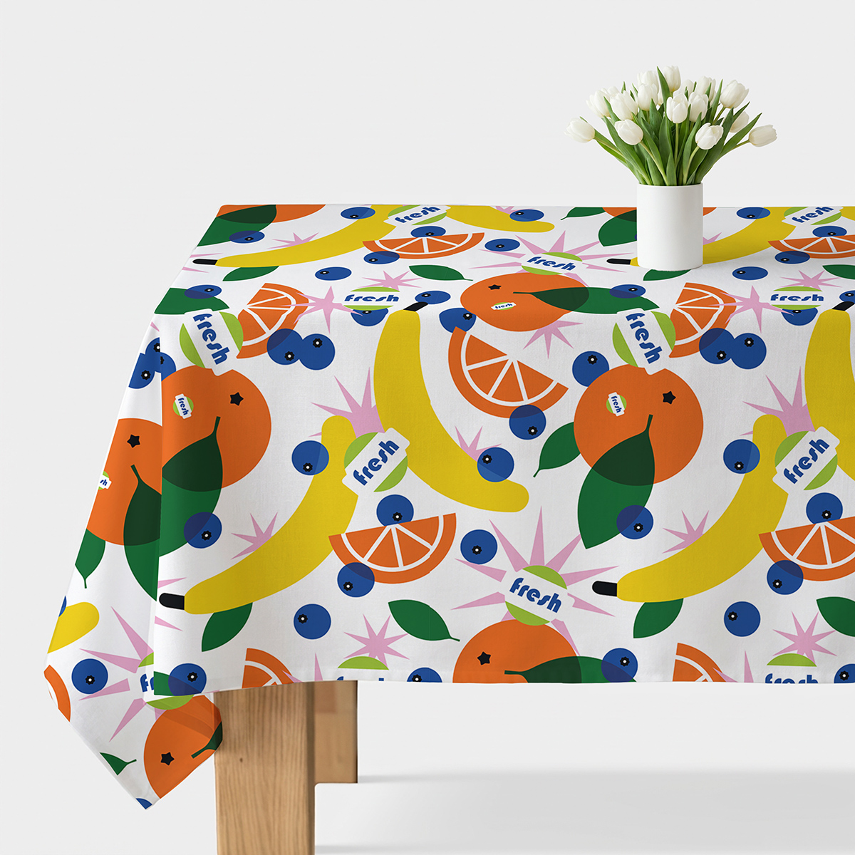 Obrus rozłożony na stole z kolorowym wzorem owoców: banany, pomarańcze i jagody na białym tle