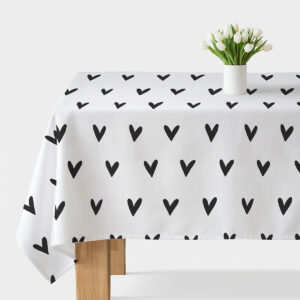 Biały obrus z czarnymi malowanymi serduszkami rozłożony na stole z wazonem tulipanów