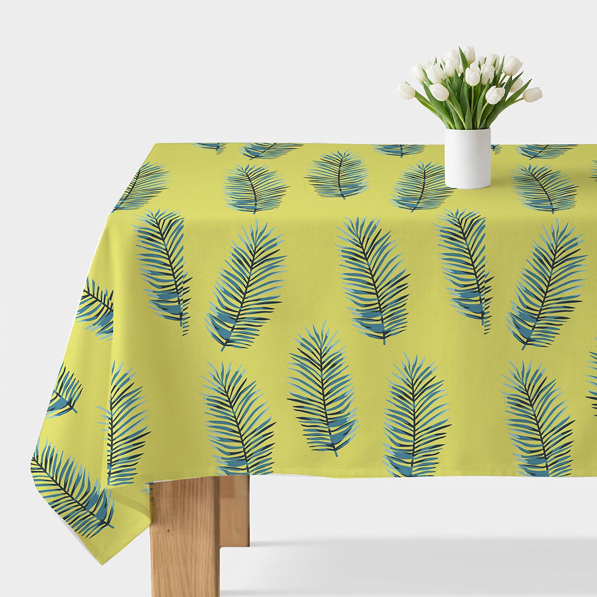 Obrus na stole z limonkowym tłem i niebieskimi liśćmi palmowymi, na środku biały wazon z tulipanami
