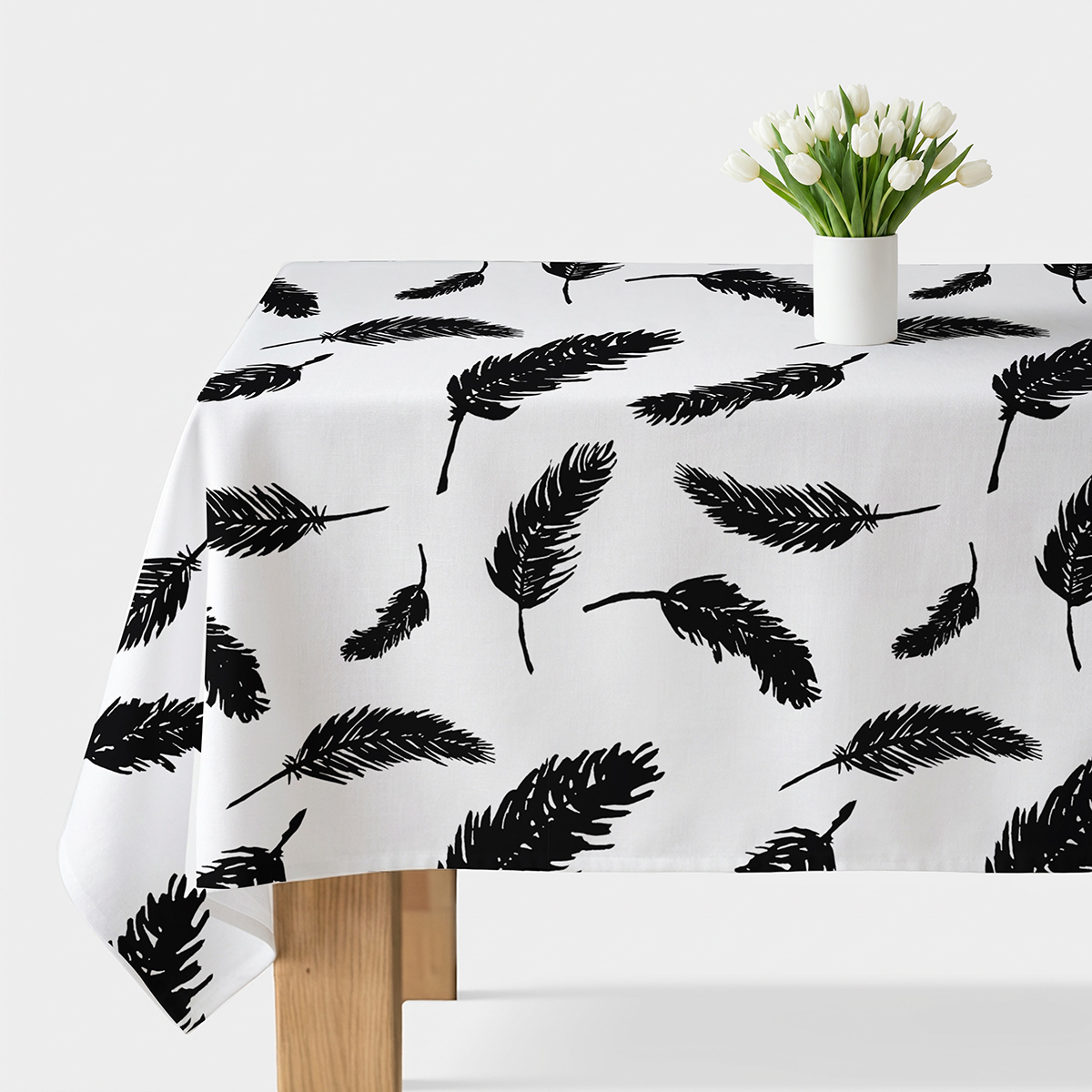 Biały obrus z czarnymi piórami rozłożony na stole z wazonem tulipanów