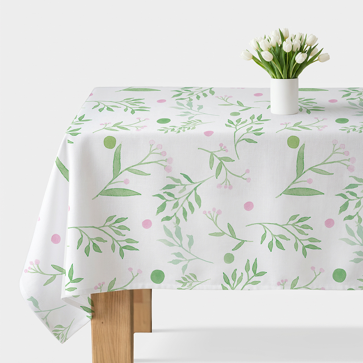 obrus z akwarelowymi zielonymi gałązkami i różowymi kropkami na jasnym stole z wazonem białych tulipanów