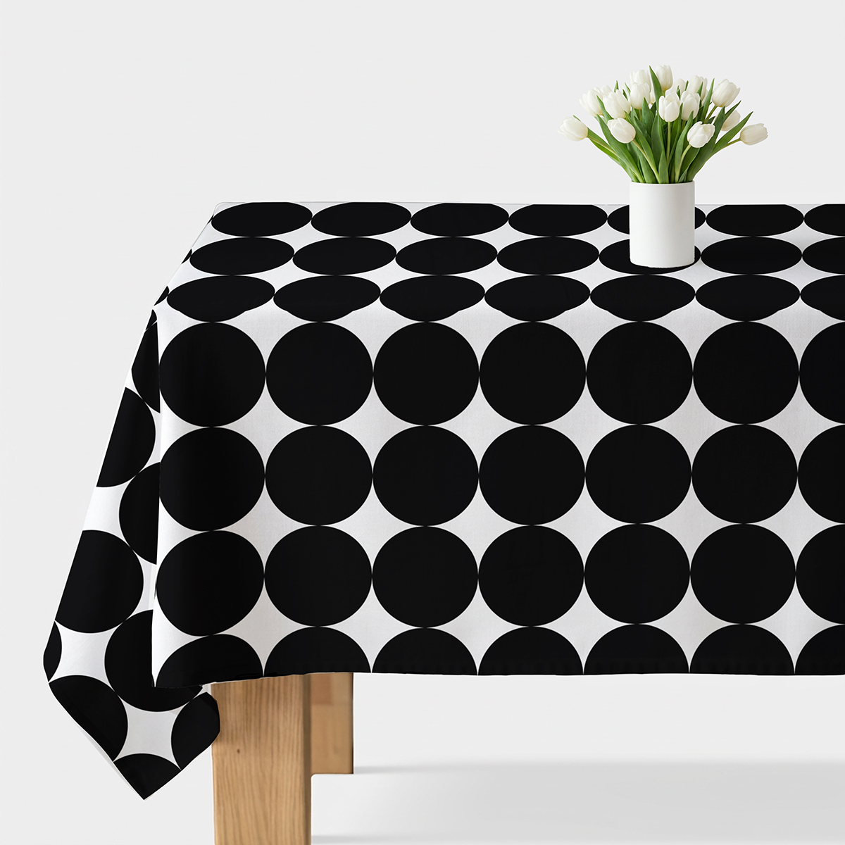 Obrus na stole z dużymi czarnymi kółkami i białym wazonem z tulipanami
