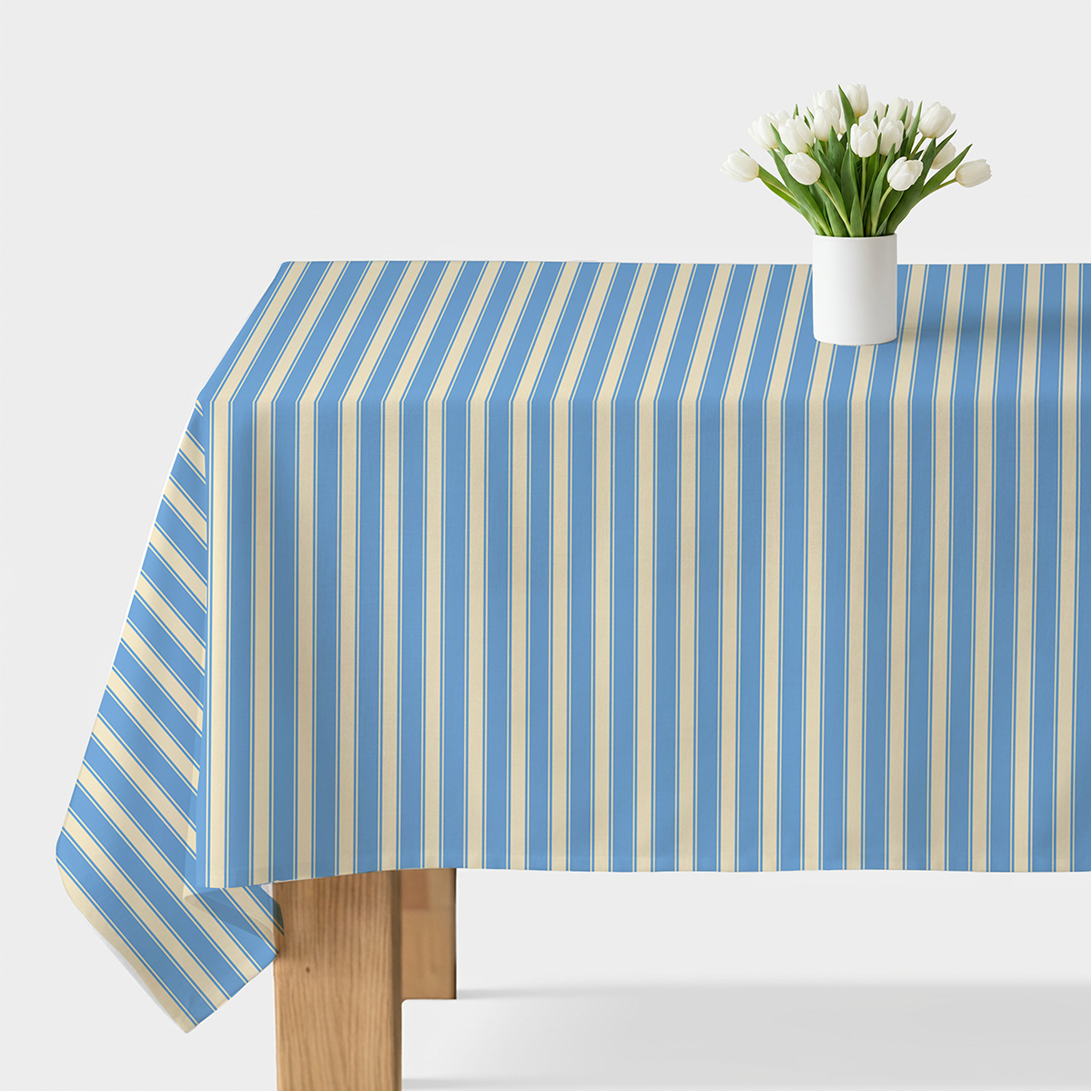 Obrus z pionowymi błękitnymi i kremowymi pasami na stole z białym wazonem i tulipanami