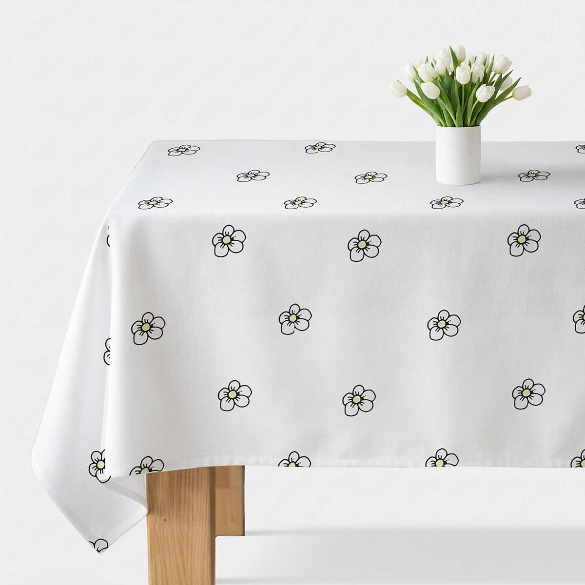 biały obrus z rozproszonym wzorem drobnych stokrotek na stole z wazonem białych tulipanów